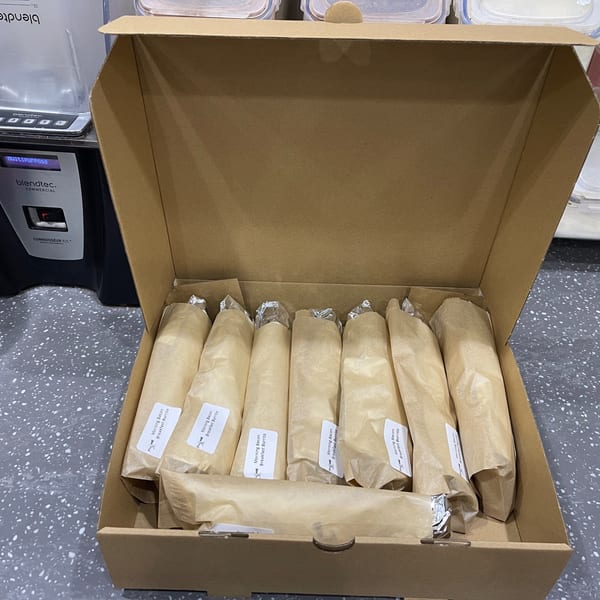 A cardboard box filled with individually wrapped "Morning Bacon Breakfast Burrito" items, ready for serving.