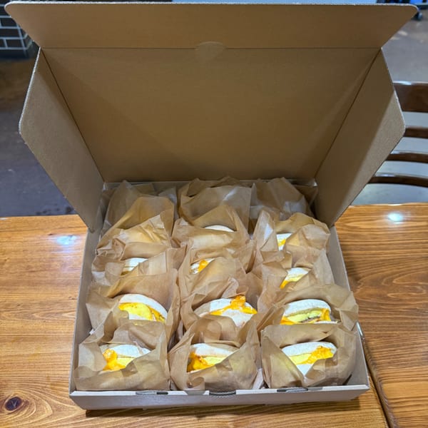 A cardboard box filled with individually wrapped breakfast sandwiches on a wooden table.