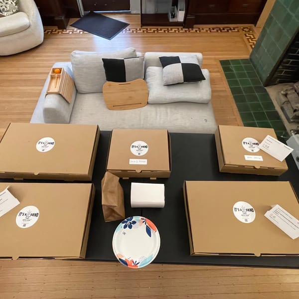 Overhead view of several "It's a Grind Coffee House" takeout boxes, bags, and a plate on a table.