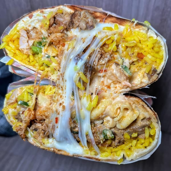 A large burrito, cut in half, revealing melted cheese, yellow rice, and meat inside.