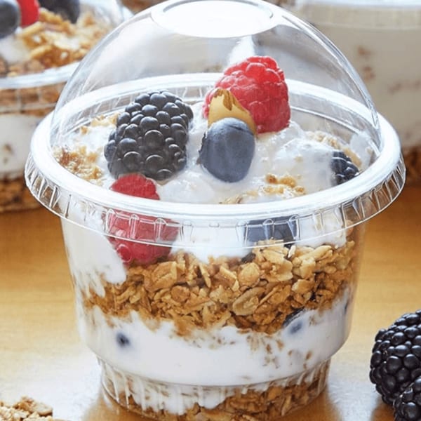 A clear plastic cup of yogurt parfait with granola, blueberries, raspberries, and blackberries.