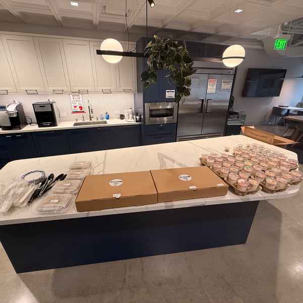 Kitchen island with two pizza boxes, plastic cutlery, and many small dessert cups.