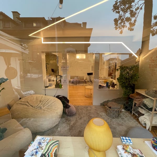 A cozy, modern living room with soft seating, a yellow lamp, and reflections of the outside.