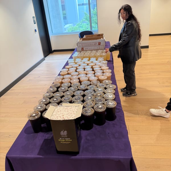 A person stands next to a long table filled with numerous drinks in plastic cups and boxes of straws.