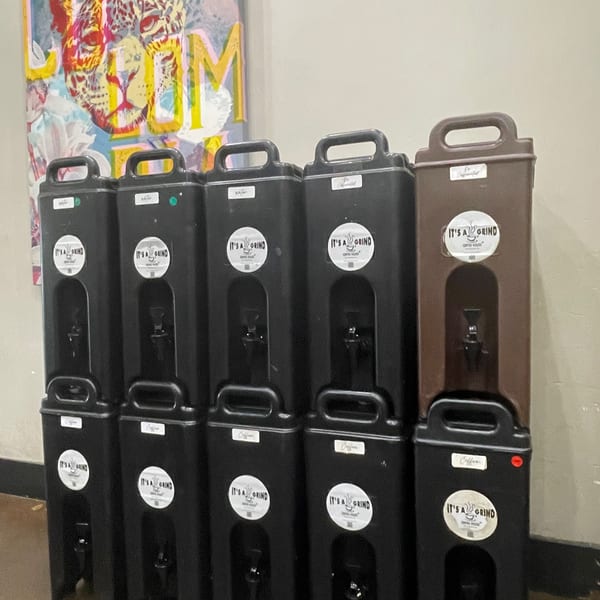 Five black and one brown "It's a Grind" coffee dispensers with a colorful leopard painting in the background.