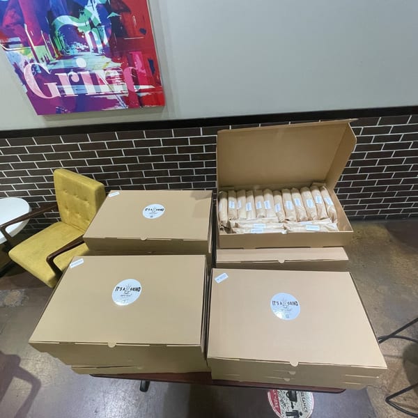Several "It's a Grind Coffee House" branded boxes, one open revealing individually wrapped pastries, on a table.