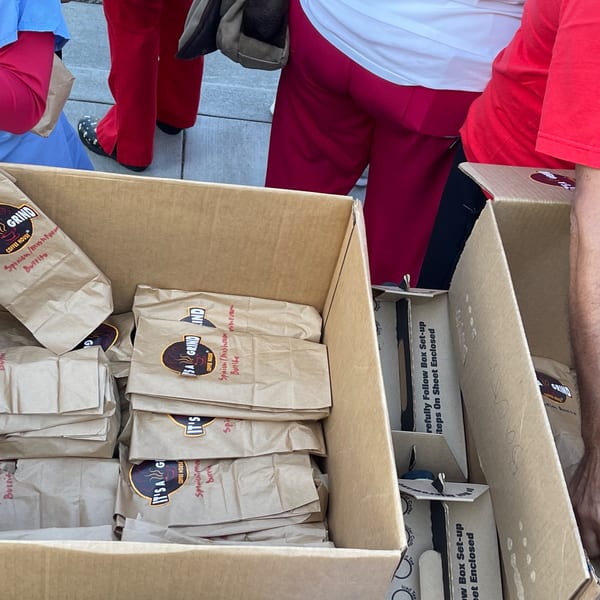 Cardboard boxes filled with brown paper bags of "It's A Grind Coffee House" spinach and mushroom burritos.